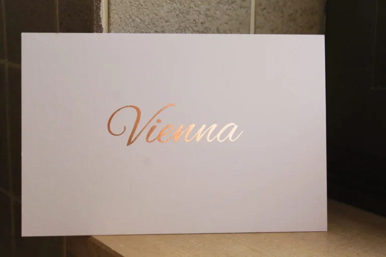 Witte geboortekaart met een naam in roségouden foliedruk op een vensterbank